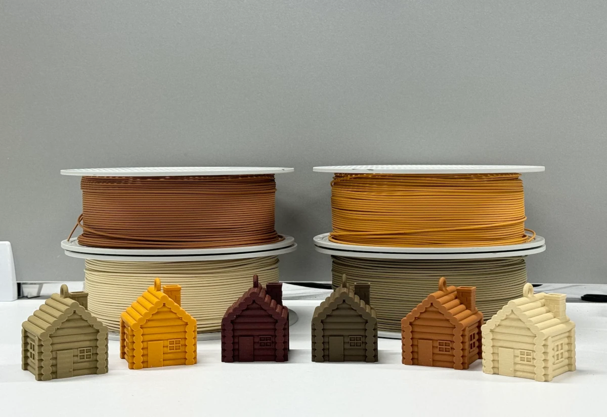 Six 3D-printed wooden cabins in front of 4 filament spools. The cabins are printed with the new Wood PLA filaments and the spools are of Wood PLA.